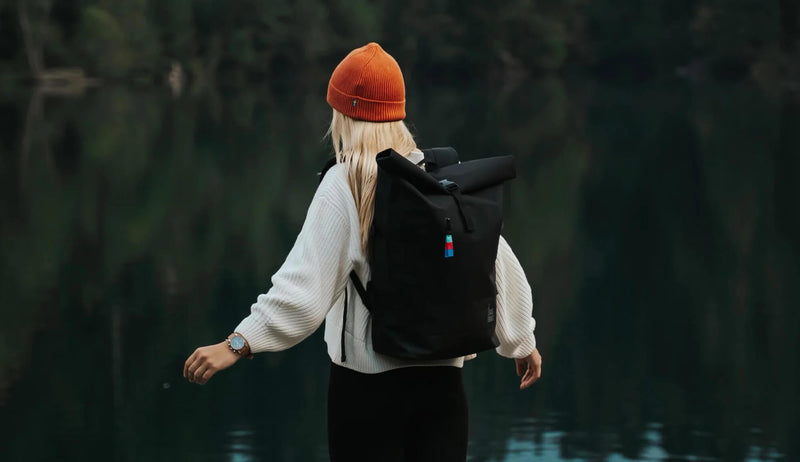 girl wearing backpack looks into a lake