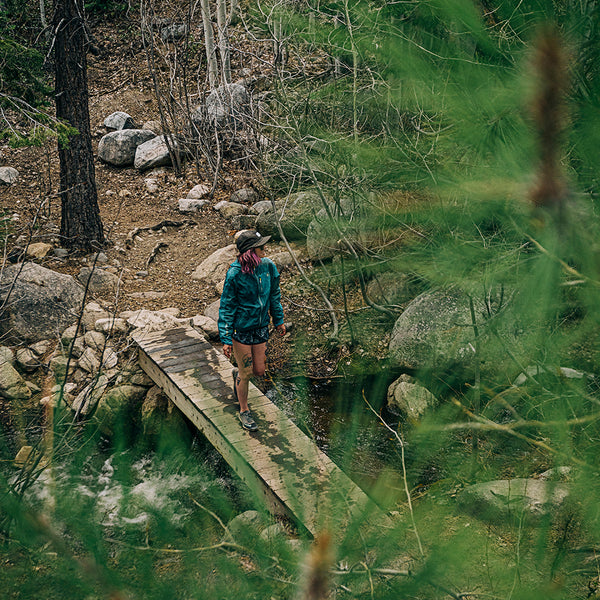 a girl walks across a wooden foot bridge over a creek