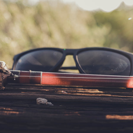 a pair of black sunglasses sitting on a log next to a fly rod