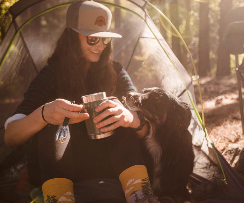 girl sitting in front of her tent with her pup looking up at her
