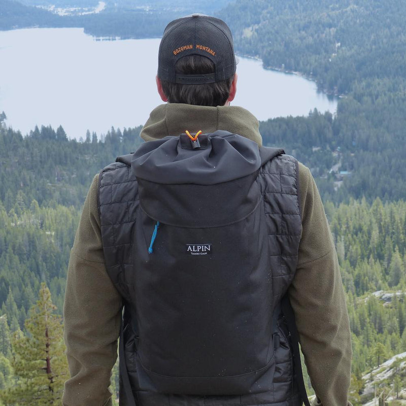 A man wears the Crag Pack overlooking a lake.
