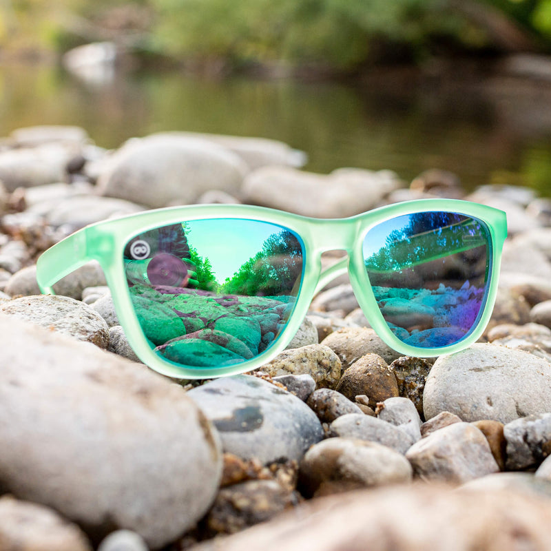 green sunglasses sitting on river rocks