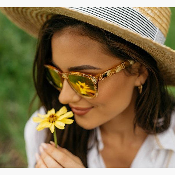 woman smelling a daisy in a straw hat wearing sunglasses