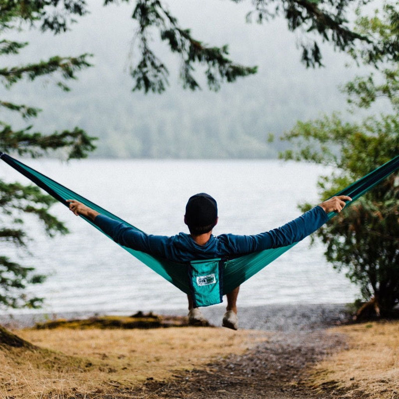 man stretched out sideways in a hammock looking towards a lake